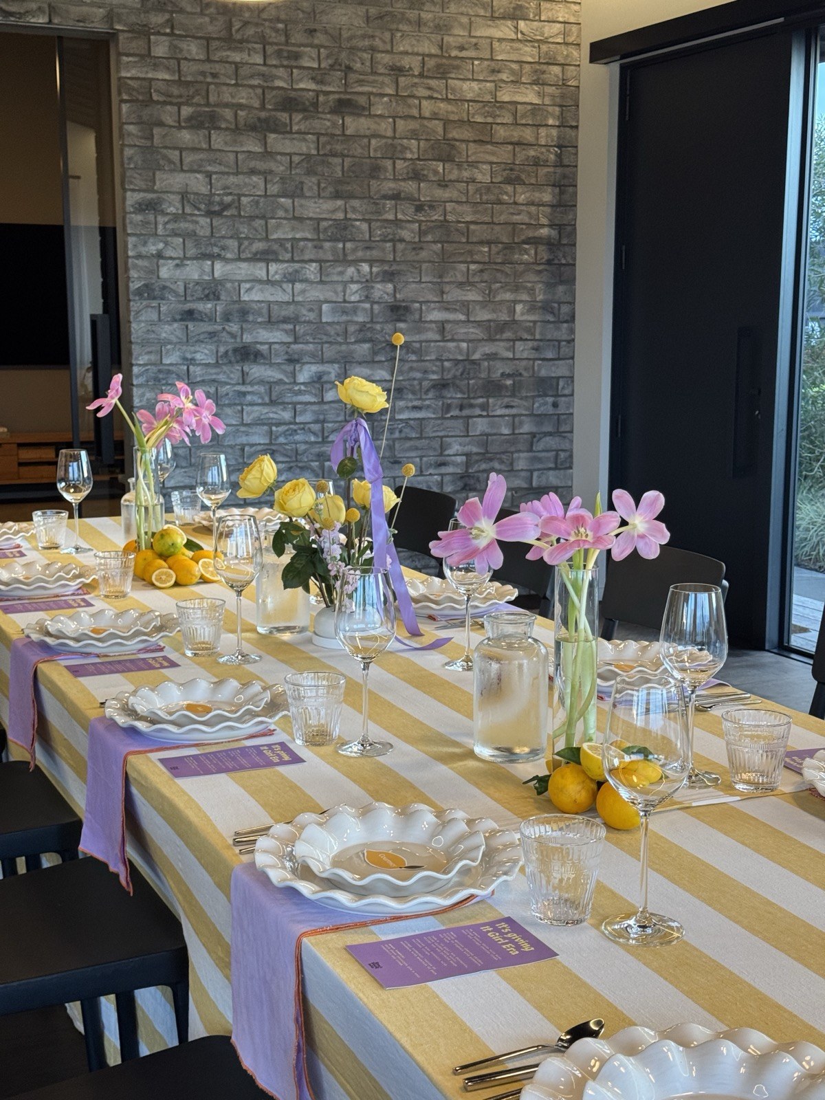 A long table set with striped runner, lemons, flowers and scalloped plates
